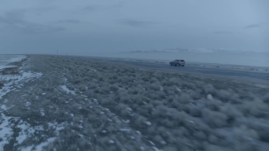 A car travels on a coastal road on a gray day