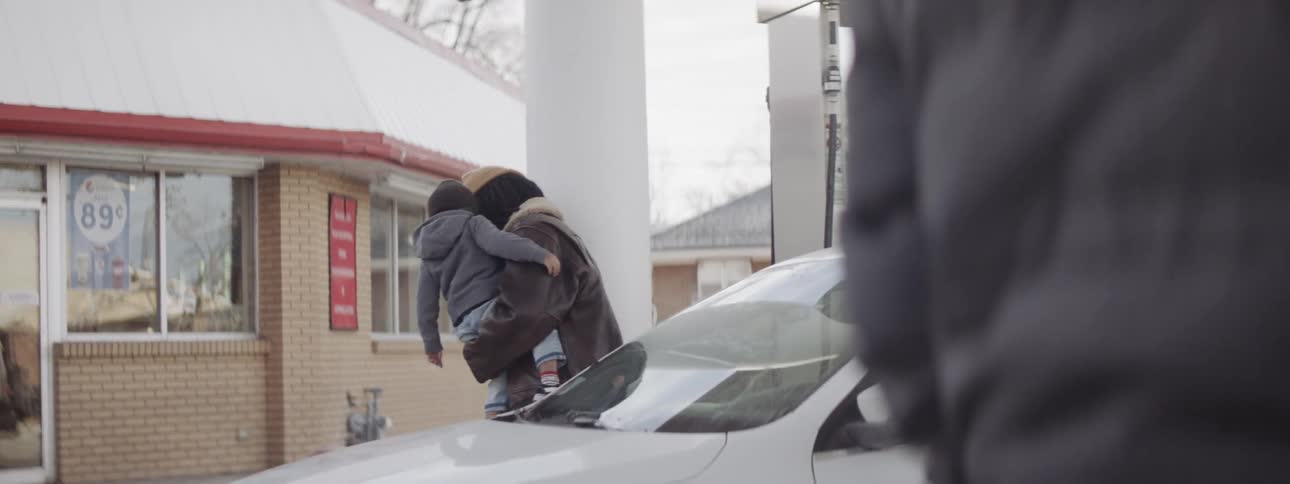Man holds a baby while cleaning his windshield at a gas station