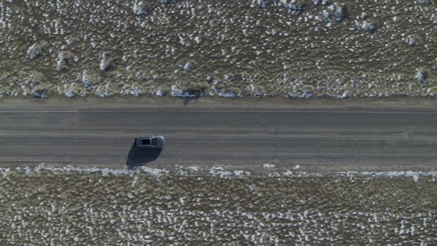 Vehicle travels down a road between snowy fields