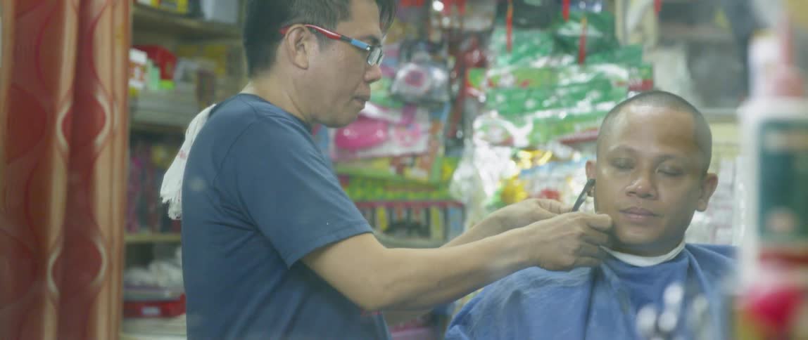 A barber is shaving a customer inside a shop in asia in daylight