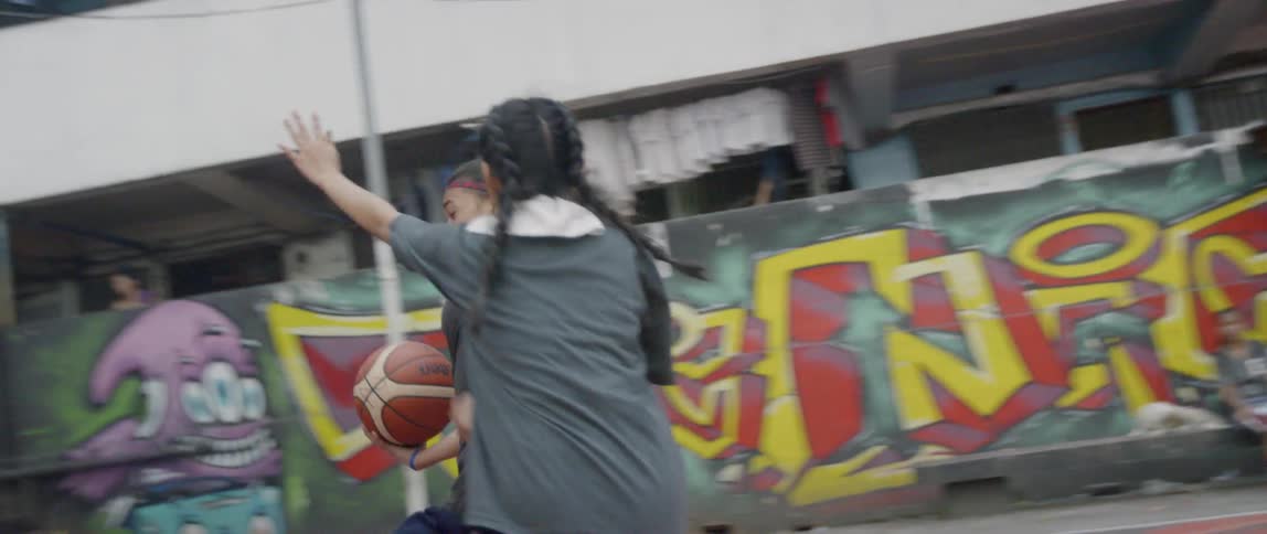 Girls are playing basketball on a court outside during the day