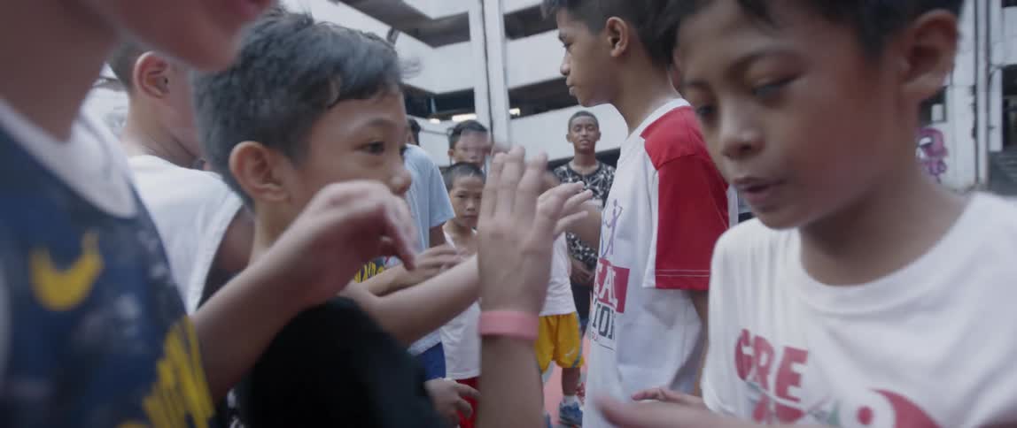 Teams of boys are shaking hands and greeting each other outside on a court in daylight