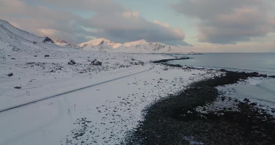 A car drives down a snowy coastal road