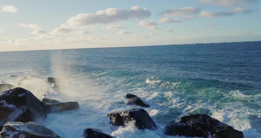 Ocean water splashes up high on large rocks