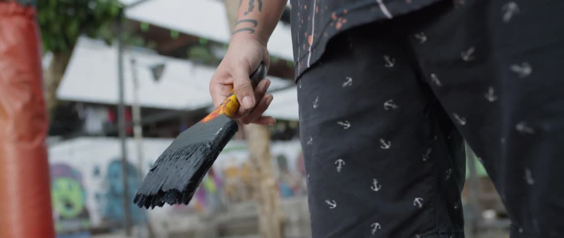 A man is holding a paintbrush outside in daylight
