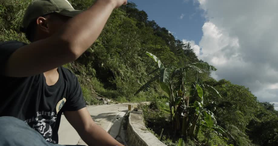 A man rides on the back of a truck on a mountain road