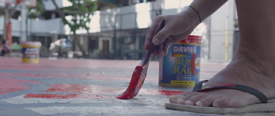A person uses a brush to paint a courtyard on a sunny day
