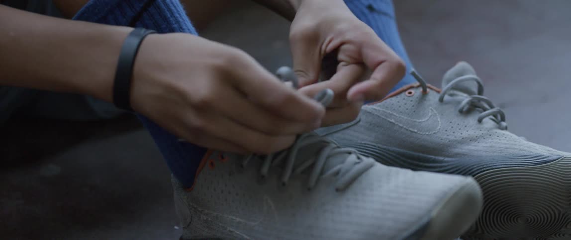 A boy sitting on the floor ties his sneakers