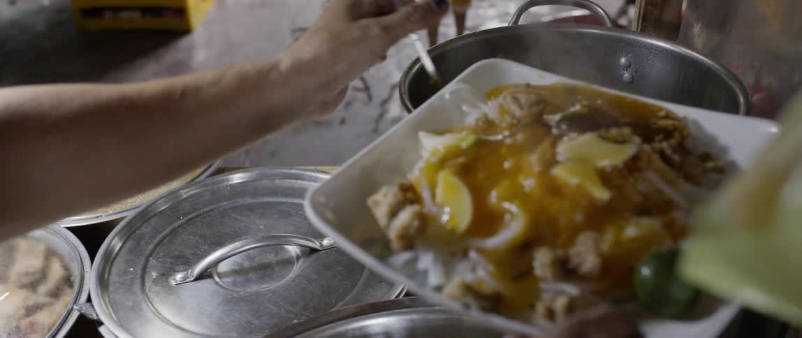 Person ladles sauce onto a plate of food