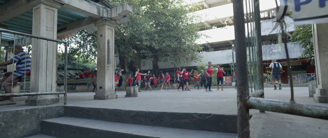 Many children wearing red shirts dance in a courtyard