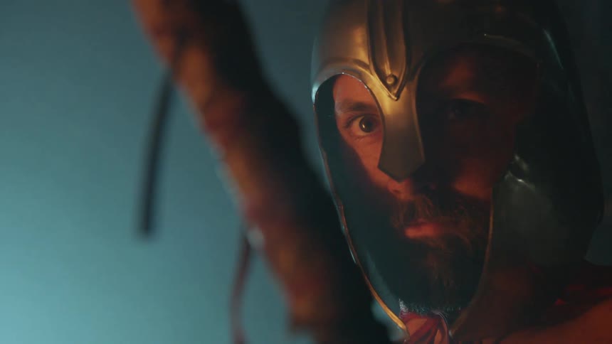 A gladiator wears a helmet near a fire