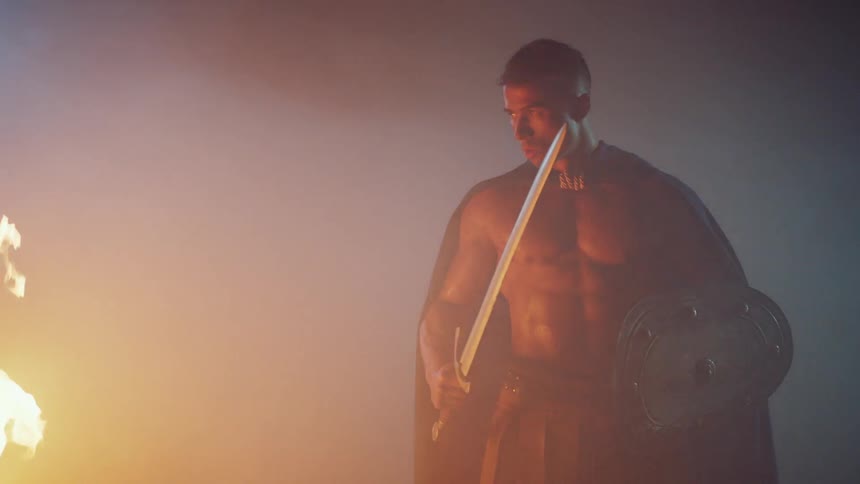 Shirtless man stands by a burning fire