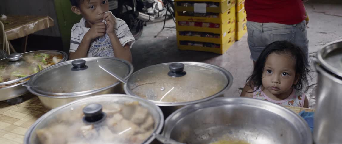 Children stand next to pots of food