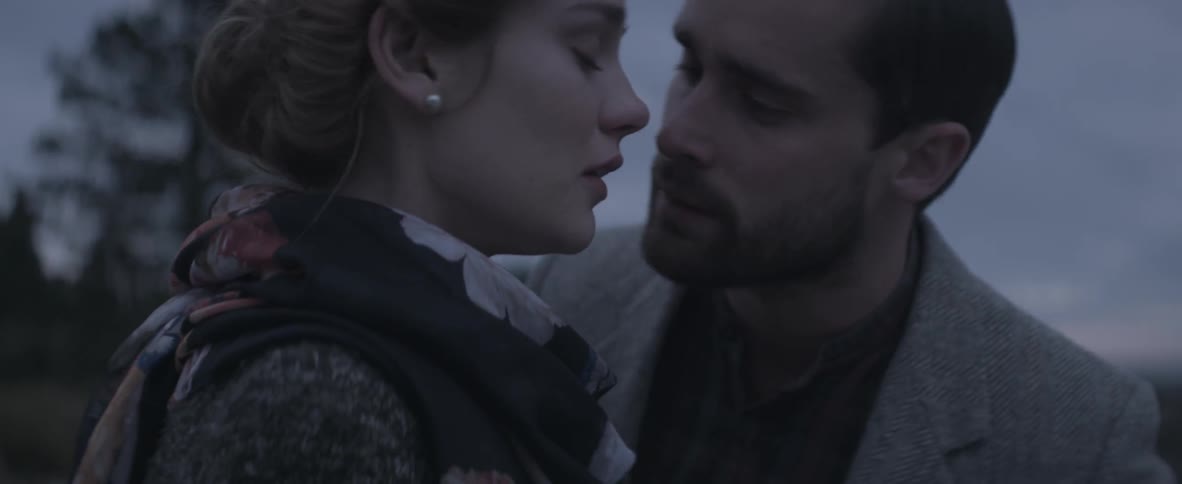 A man kisses a woman on the cheek while both are standing outside