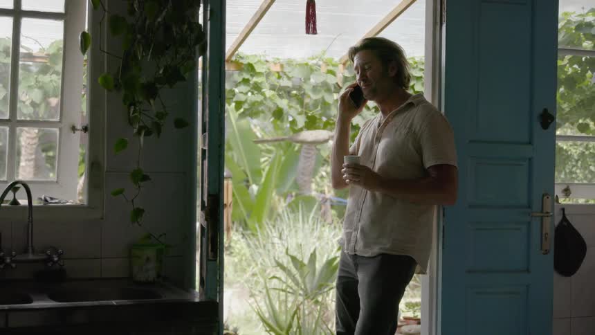 Man leans on a door frame as he talks on a cellphone