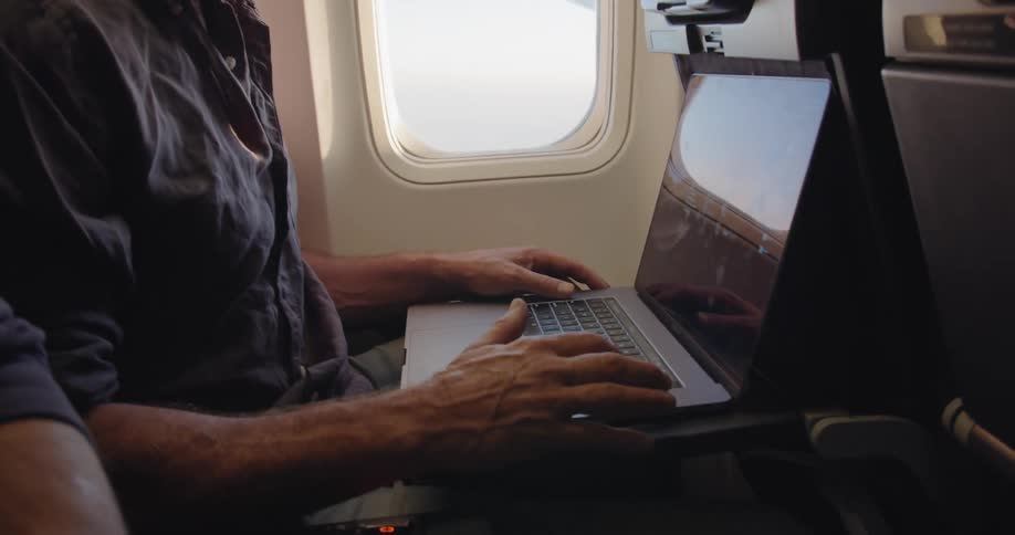A man types on a laptop during a flight