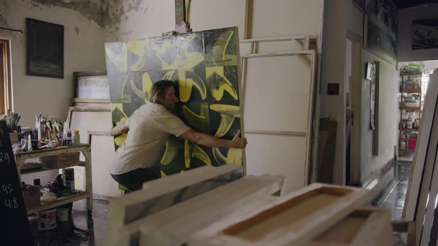 An artist removes a canvas painting from its easel