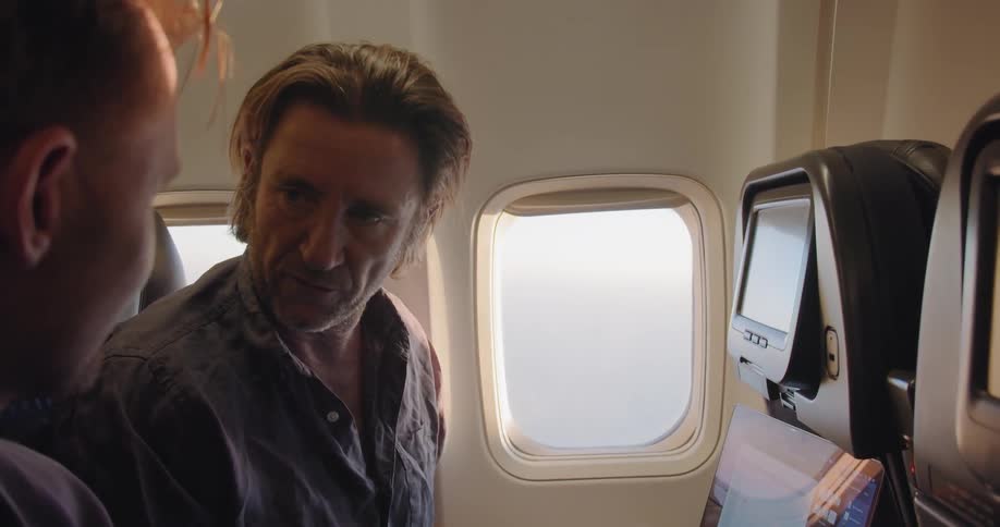 Two men talk while flying on an airplane