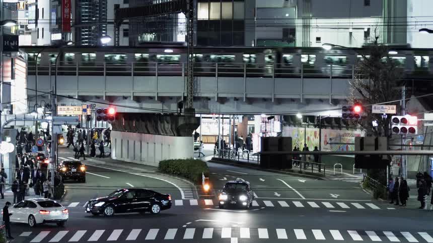 A train passes overhead as people and traffic move through an intersection