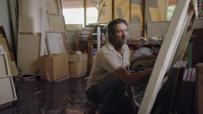 A man is admiring pictures sitting on the ground in an art studio in daylight