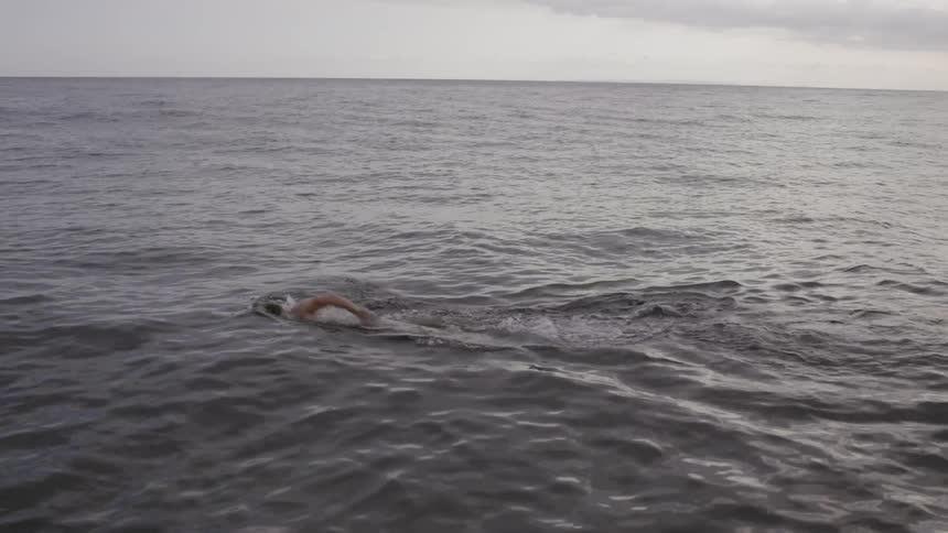 A man is swimming in the ocean on a cloudy day