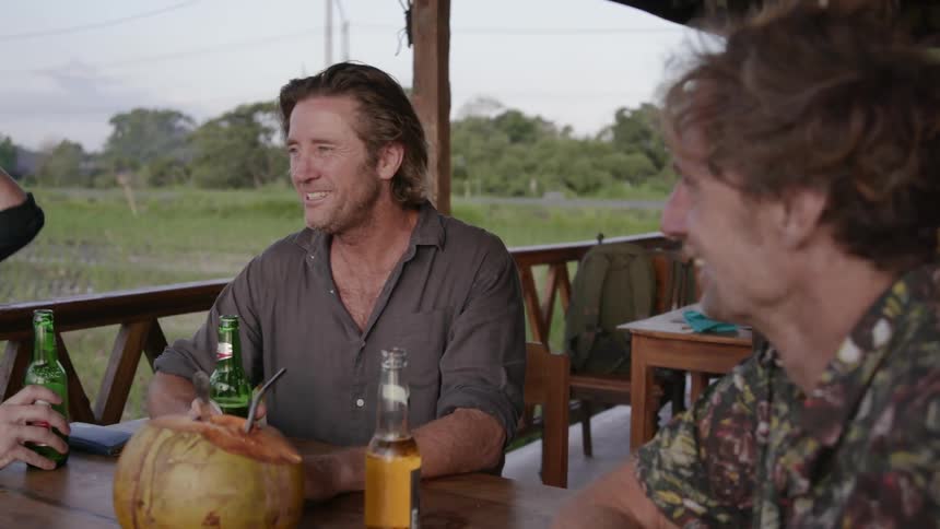 Three men sit around an outdoor table with bottles of beer