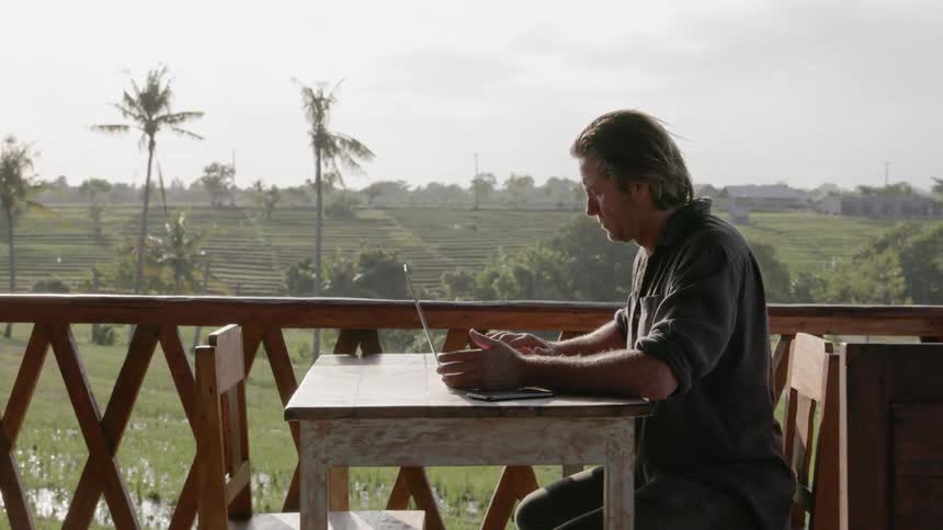 Man types on a laptop on a patio