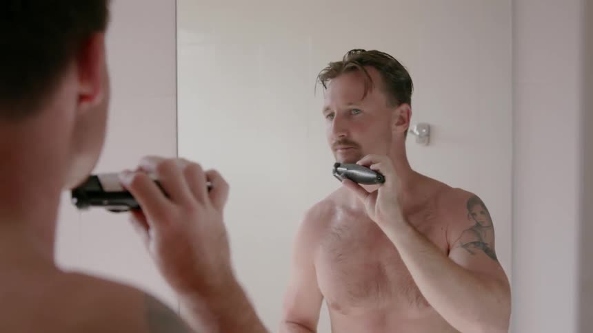 Man shaves his face while looking in the mirror