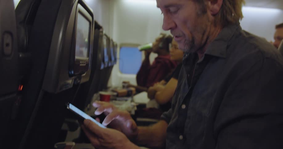 A man on an airplane texts on his phone