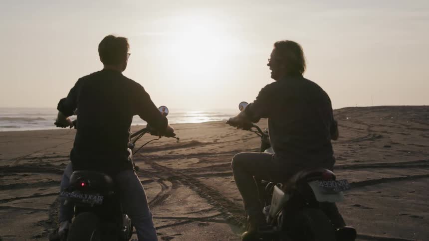 Motorcyclists ride on a beach at sunset