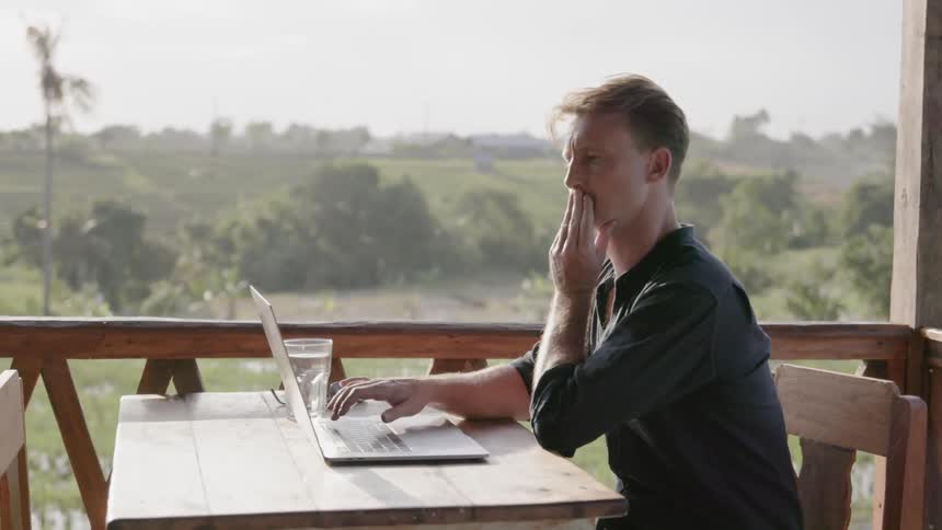 Man types on a laptop on a patio