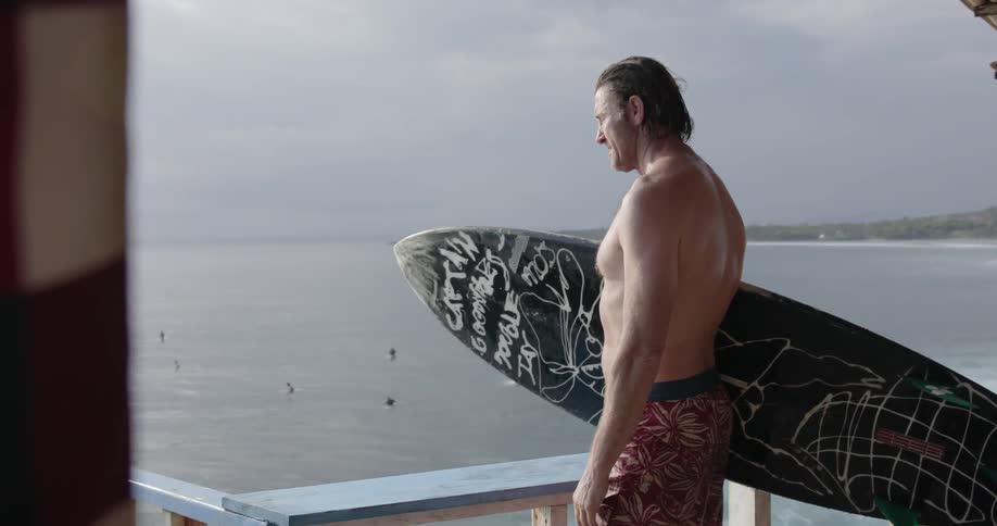 A man holds a surfboard by the shore