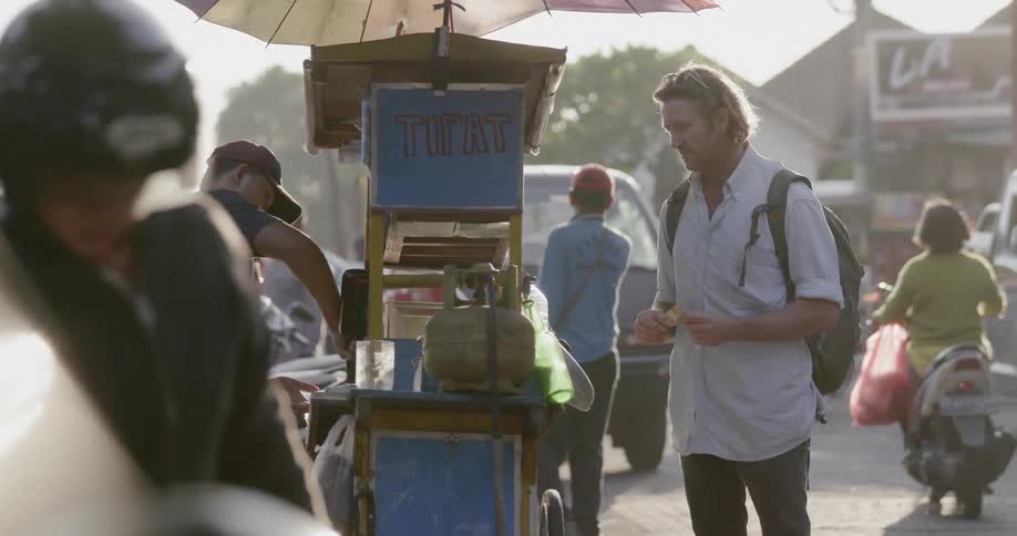 A man is buying food from a street vendor outside in daylight