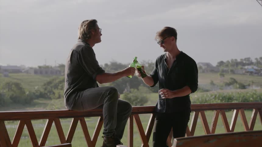 Two men drink and talk on a patio