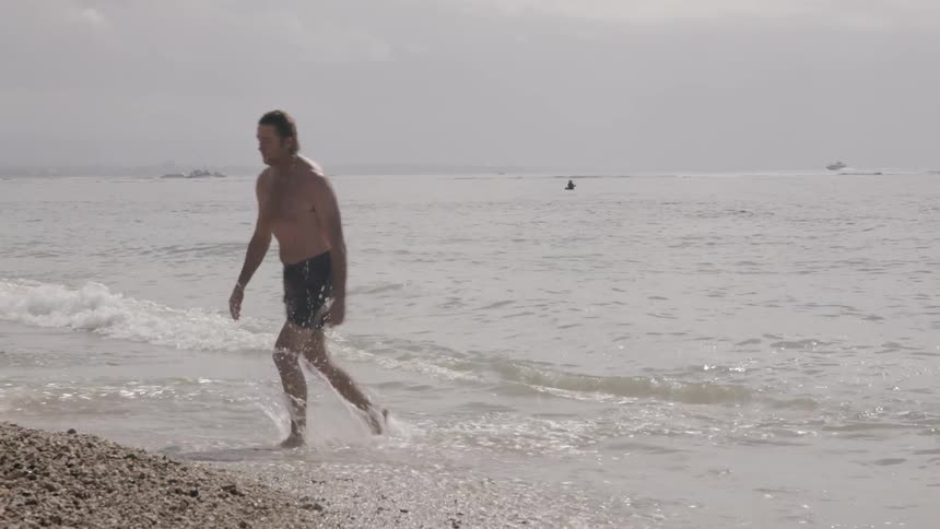 Man walks in the water onto the beach on a sunny day
