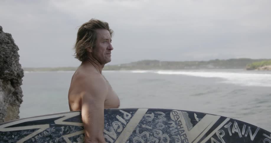 A man carrying a surfboard is watching the waves on a cloudy day