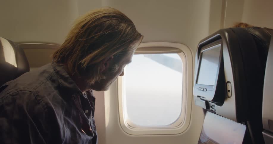Man sits in an airplane as he types on a laptop