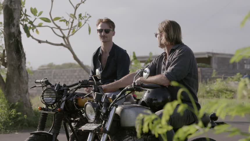 Two motorcyclists talk while parked on a road