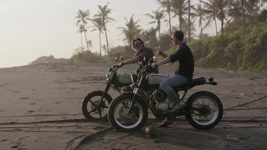 Two motorcyclists talk while parked on a beach