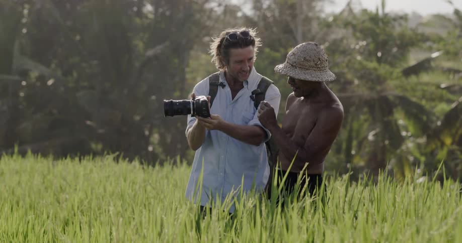 A man shows another man his camera in a field