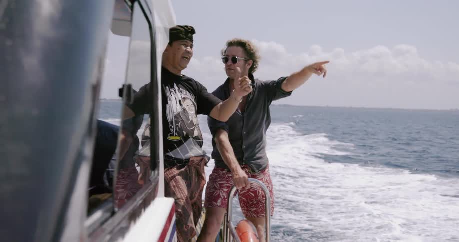 Two men talk while standing on the edge of the moving boat