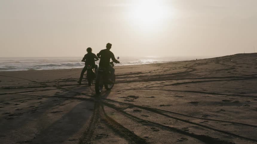Motorcyclists ride on a beach at sunset