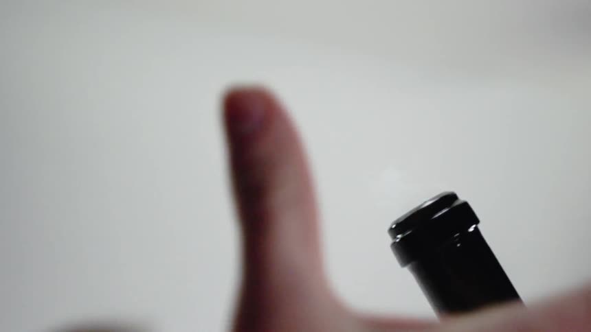 A person pops a champagne bottle cork with their thumb
