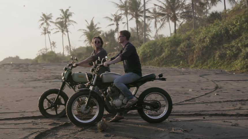 Motorcyclists ride on a beach at sunset