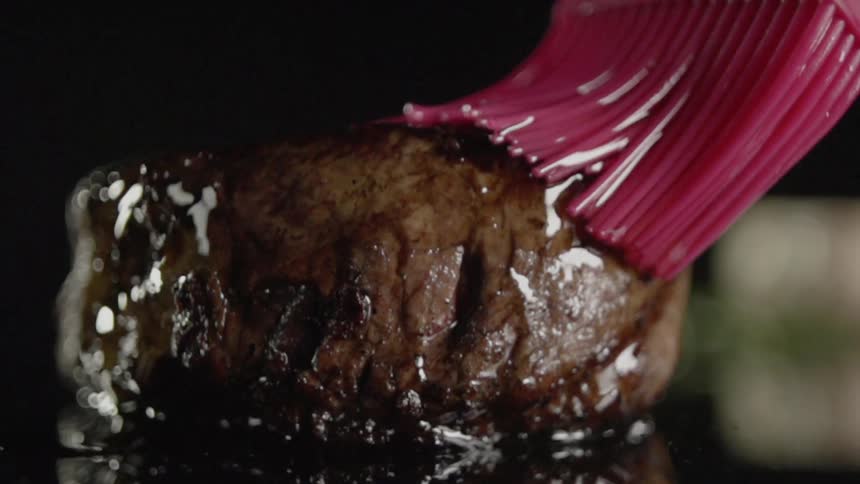 A cooked steak is basted with butter
