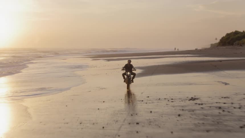 Man rides motorcycle along beach