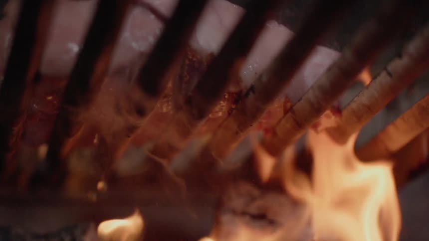 Meat sizzles on a grill with flames underneath