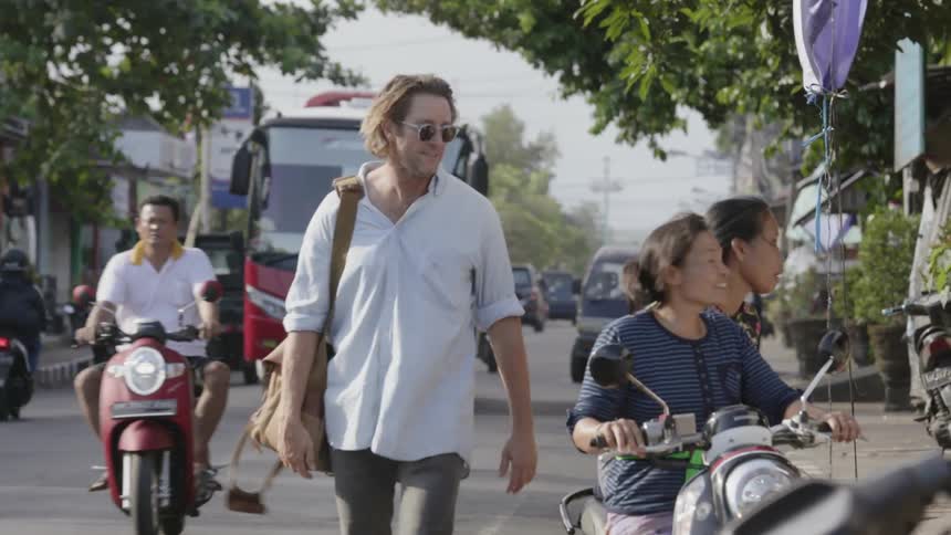 A man waves to two passing riders on a scooter