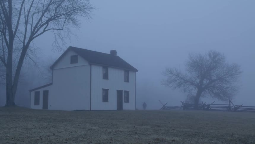 A person walks towards a house in the fog