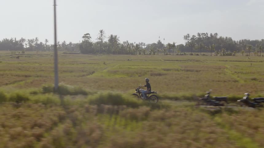 A man rides a motorcycle through farmland